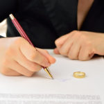 Wife signing divorce agreement with wedding ring on contract