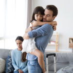 little girl hugging dad with mom in background