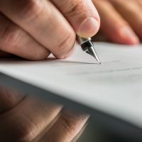 Closeup of male hand about to sign a will or a trust.